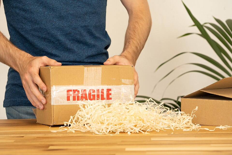 Lezárt, FRAGILE szalagos kartondoboz, előtte csomagolóforgács